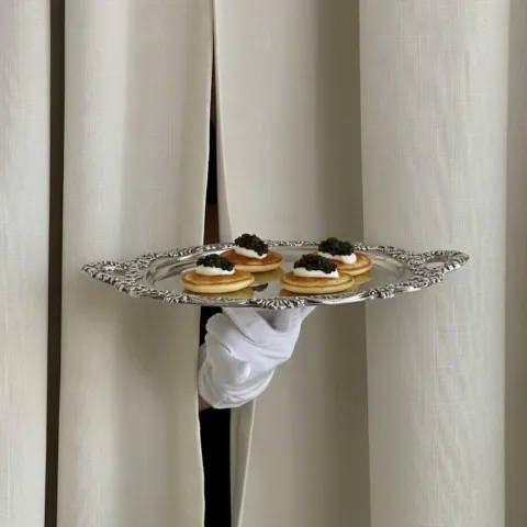 Blinis mit Kaviar stehen auf einem silbernen Tablett.